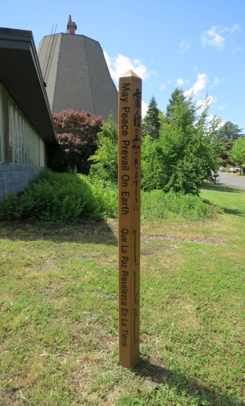 Hexagonal pole, approximately 6 feet tall, with inscribed writing in multiple languages with the church in the background 